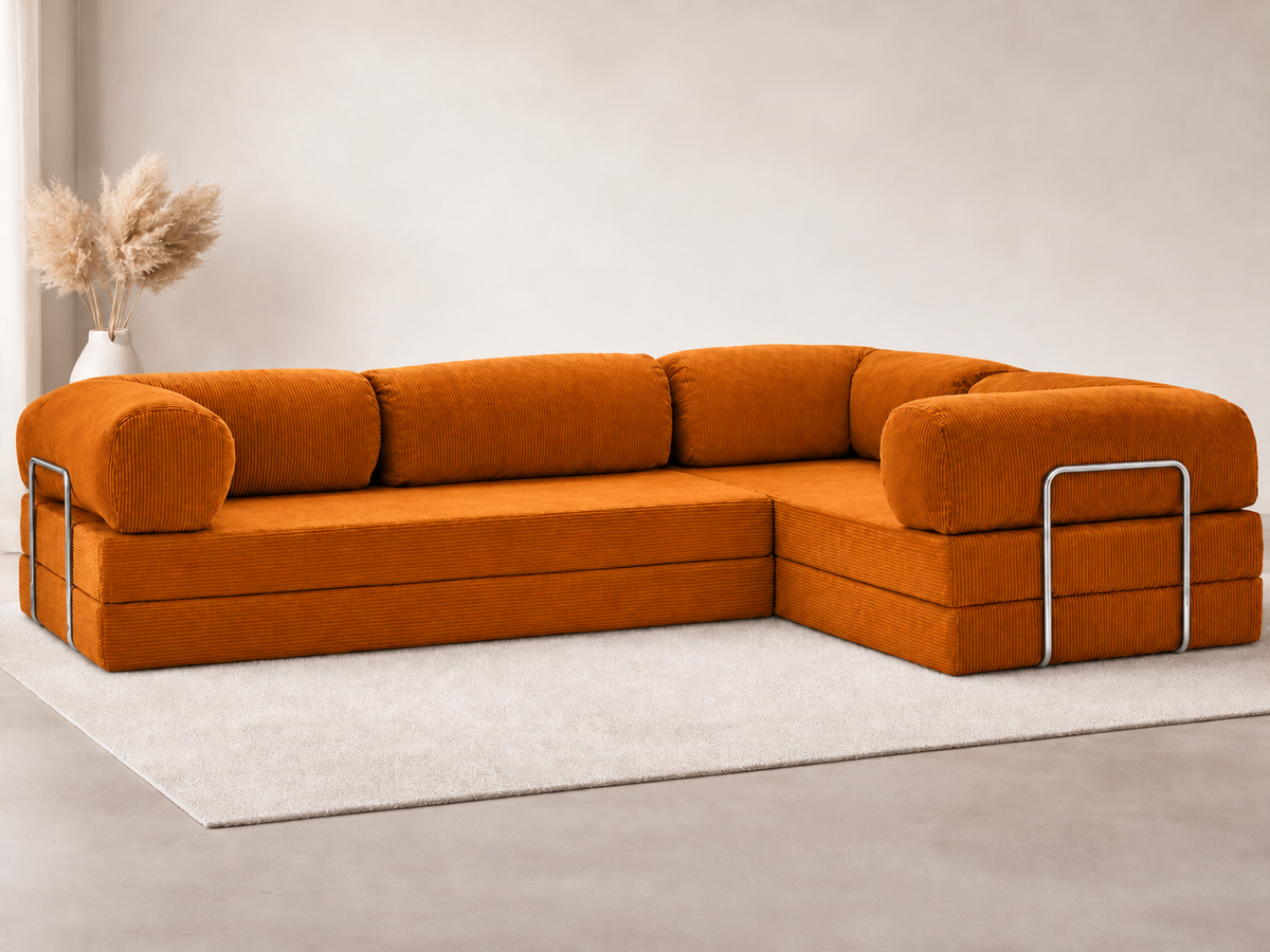Confex Corner Orange Sofa arranged on a cream rug in a neutral living room, with rounded arms, orange back cushions and slim metal detailing around the outer ends beside a vase of dried grasses.