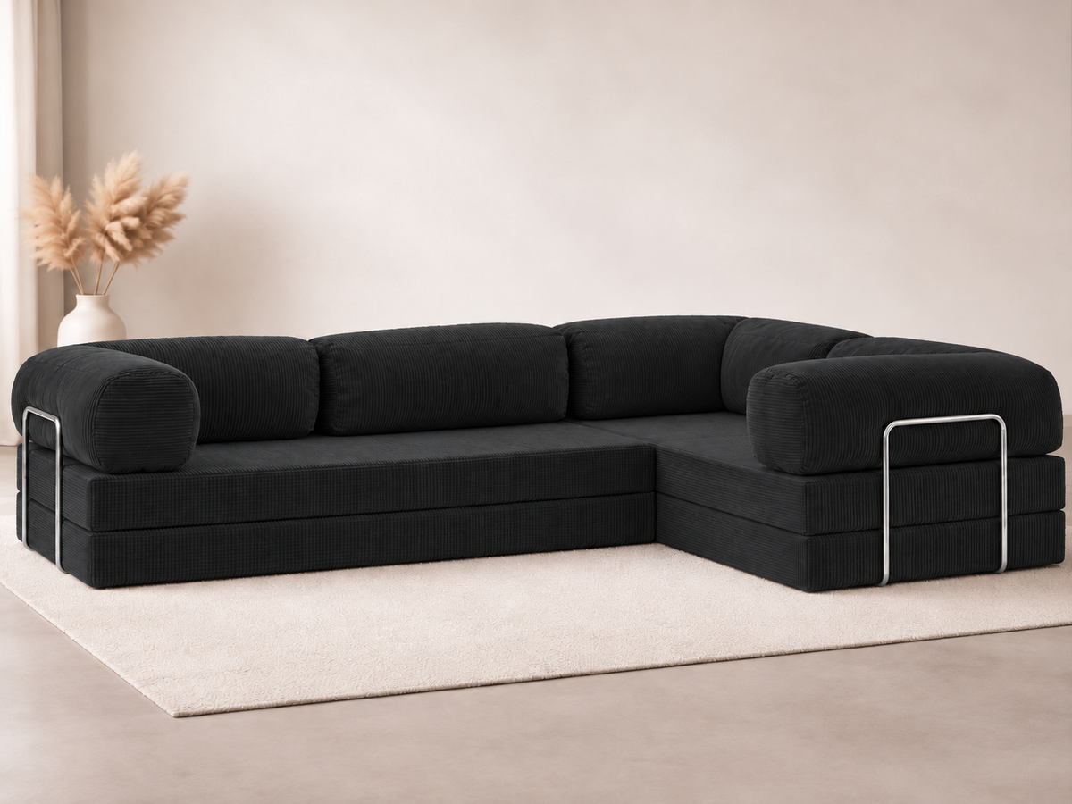 Black upholstery contrasts with a cream rug beneath the Confex Corner Black Sofa in a pale living room, with rounded arms, metallic outer details and a vase of dried foliage beside the seating area.